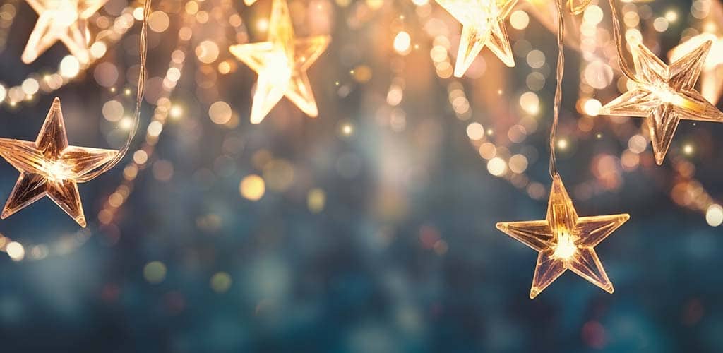Leuchtende Sternlichter hängen in einer festlichen Dekoration vor einem unscharfen, funkelnden Hintergrund in Blau- und Goldtönen.