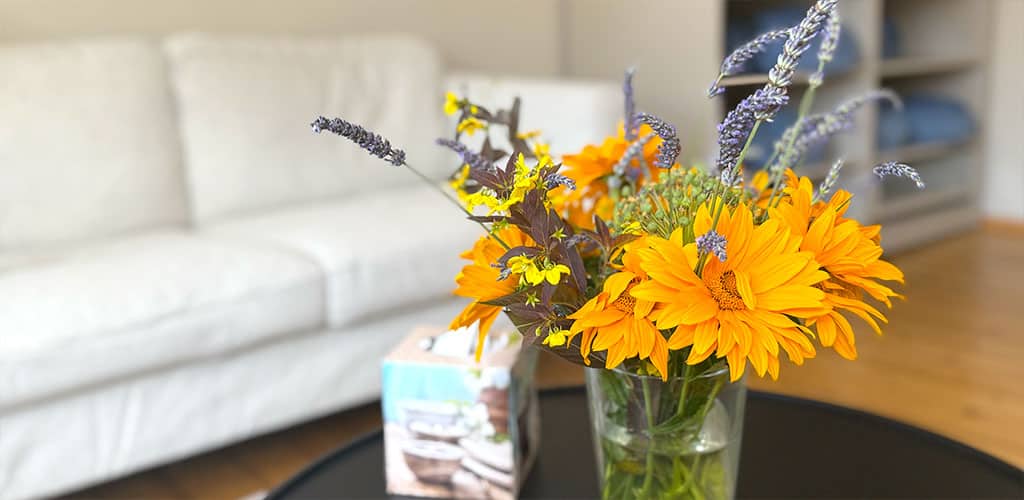 Nahaufnahme eines Sonnenblumenstraußes mit Lavendel in Gelb und Violett, im Hintergrund Regale mit blauen Yogakissen.