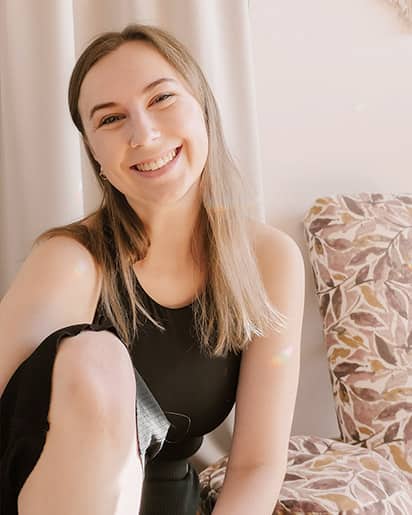 Yogalehrerin Yvonne Schatz sitzt lächelnd vor einem hellen, neutralen Hintergrund mit einem gemusterten Yogabolster – freundliche, entspannte Atmosphäre.