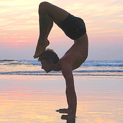 Yogalehrer Christian Klix praktiziert einen Handstand mit Rückenbeuge am Strand bei Sonnenuntergang, mit ruhigem Meer und farbigem Himmel im Hintergrund.