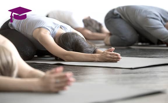 Yogaschüler knieen auf ihren Matten und haben mit flach vorgebeugtem Oberkörper und nach vorne gestreckten Armen ihre Köpfe auf der Matte abgelegt und praktiziert Yin Yoga