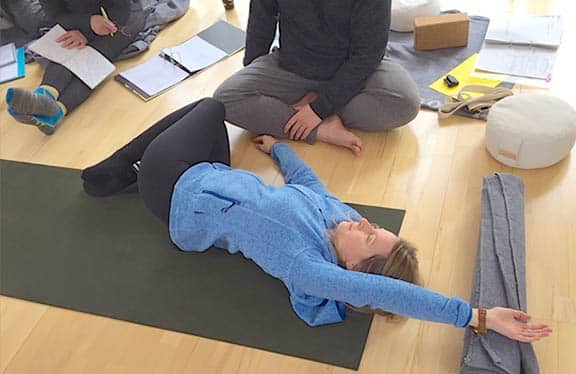 Wolfgang Riedl demonstriert Assists und Adjusts für Yin Yoga Asanas an einer auf dem Rücken und mit ihrem Kreuz auf einem Yogablock liegenden Kursteilnehmerin