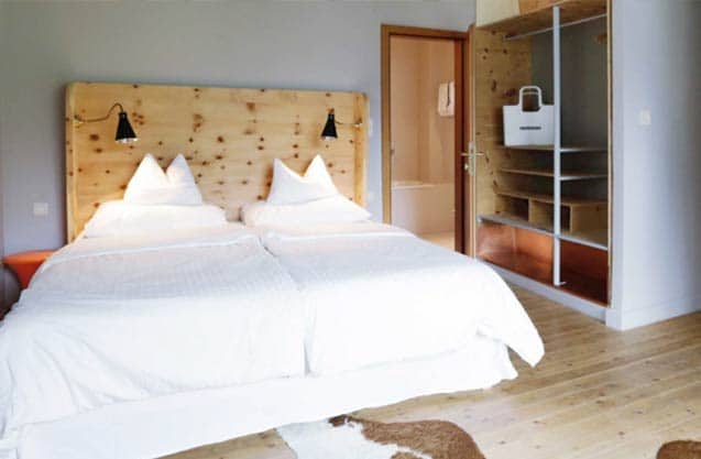 Blick in ein großes Hotelzimmer mit weißen Wänden,hellem Holzdielenboden mit Kuhfellteppich, großen offenen Kleiderschrank, auf die gläserne Tür zum Badezimmer (Foto: Copyright by © Hotel Miramonte/Bad Gastein)