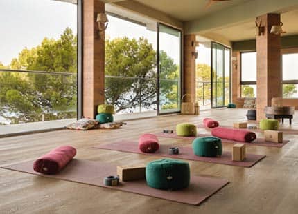 Der große mit Holzdielen ausgelegten 'Yoga Soul Room' mit auf dem Boden liegenden Yogamatten und -zubehör und großen bodentiefen Panoramafenstern mit Blick auf das Meer
