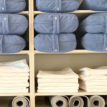 Regal im Propsraum von Yogaplus Studio Mainz mit ordentlich gestapelten blauen Bolstern, weißen Handtüchern und aufgerollten Yogamatten.