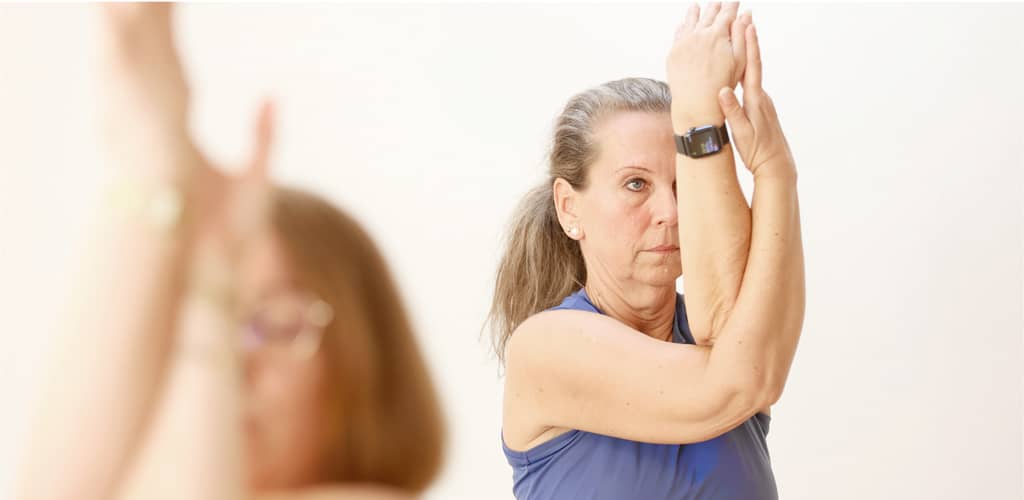 Frau in blauer Sportkleidung hebt die Arme in Gebetshaltung nach oben, konzentriert im Yoga-Kurs.