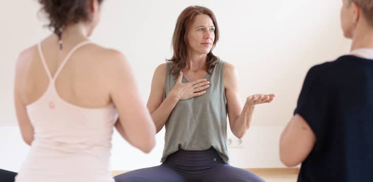 Dozentin Sonja Schwarz-Niemeyer steht während einer Meditationspraxis der Yogalehrerinnenausbildung zwischenn ihren Schülern in gibt Anleitungen