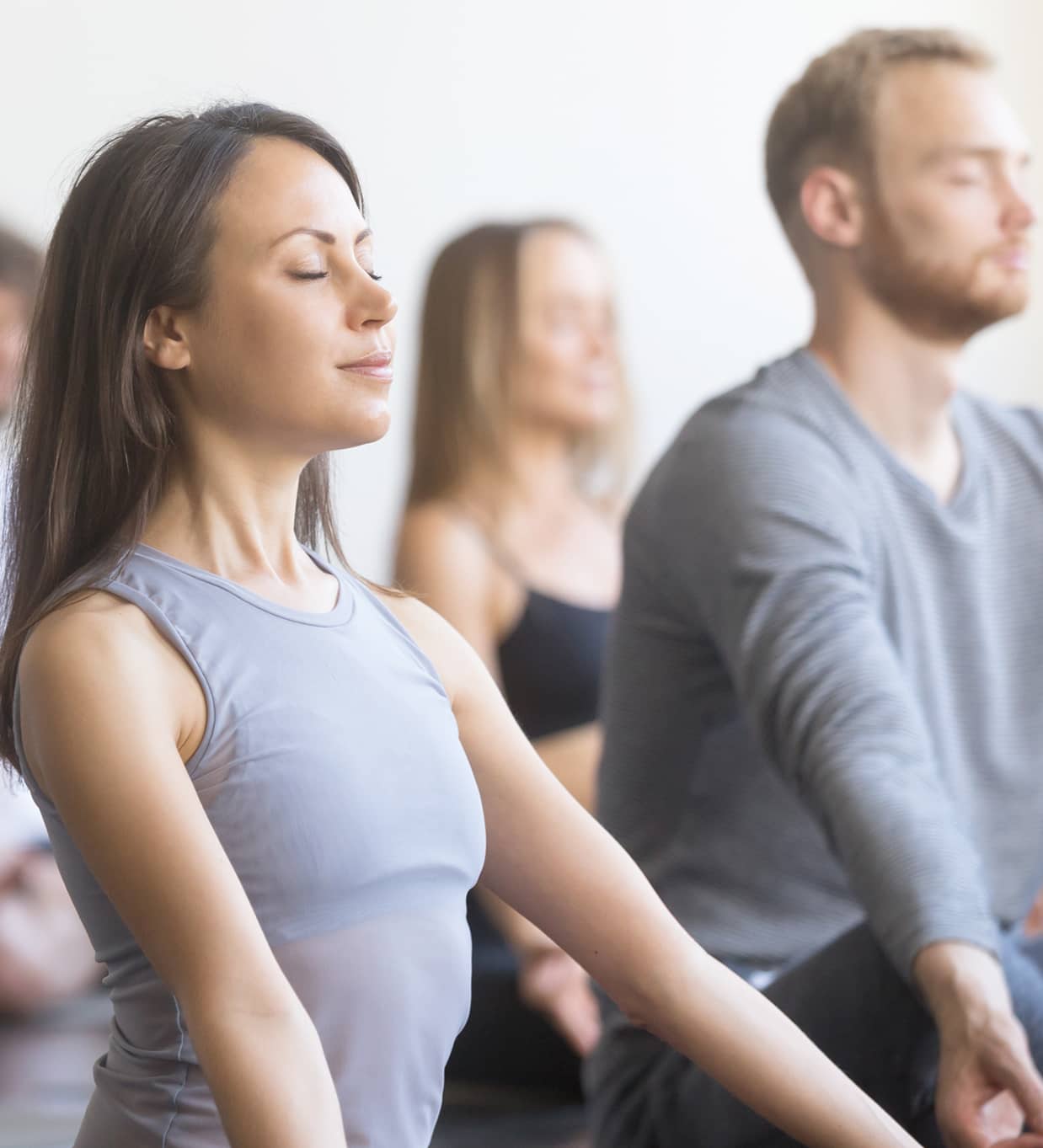 Gruppe von Menschen sitzt im Schneidersitz mit geschlossenen Augen und aufrechter Haltung in einer Yogastunde.