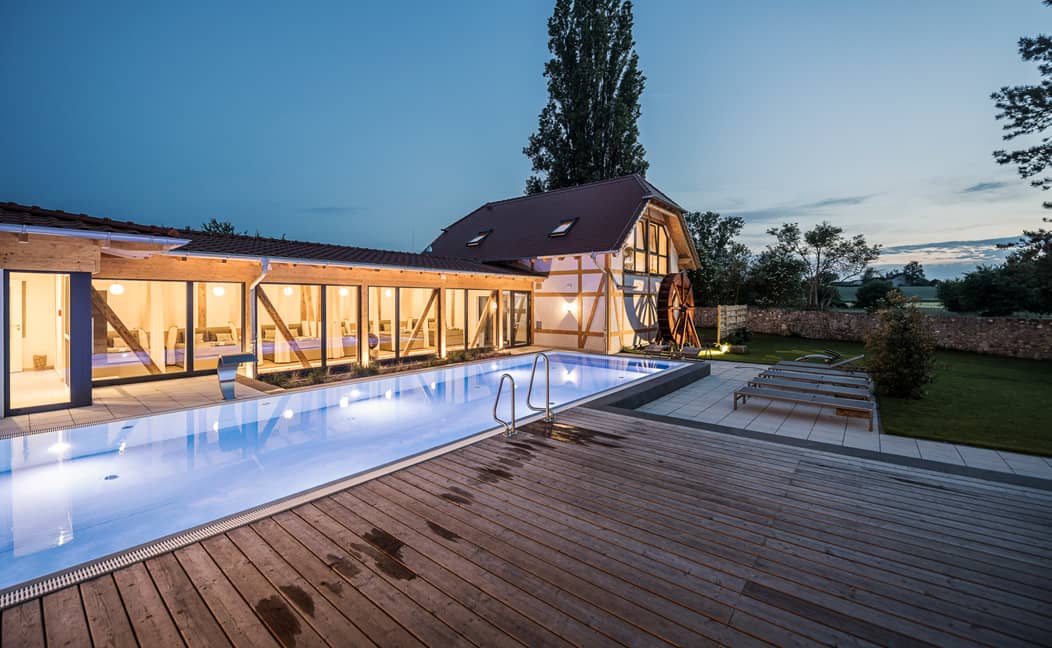 Stimmungsvoll beleuchtetes Poolhaus im SPA-Bereichs von Jordan's Untermühle mit Glasfront und Außenbecken bei Abenddämmerung.