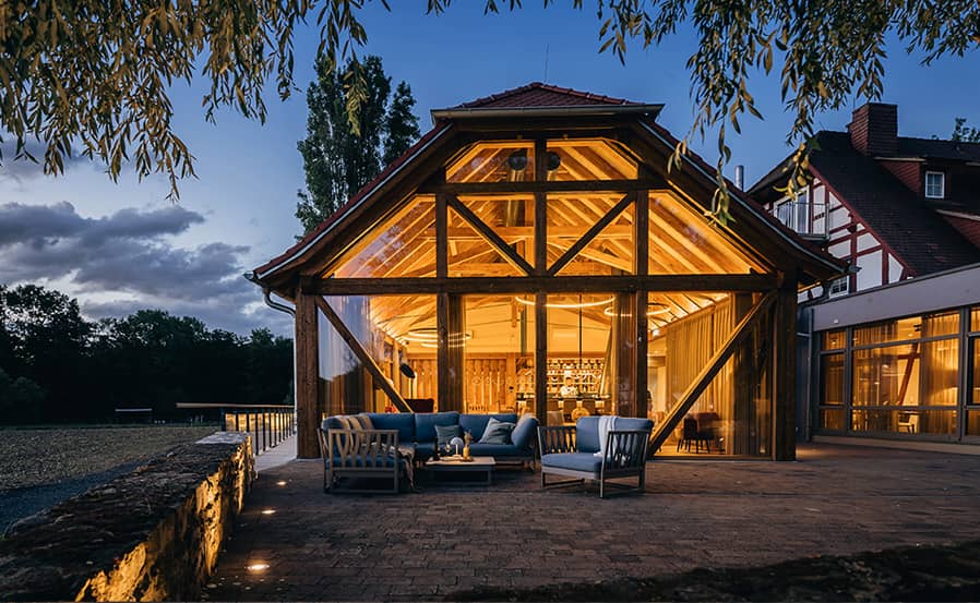 Stimmungsvoll beleuchtetes Fachwerkgebäude des SPA-Bereichs von Jordan's Untermühle mit Glasfront und gemütlicher Außensitzgruppe bei Abenddämmerung.