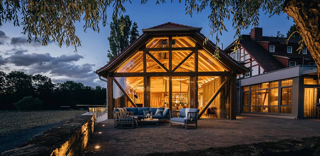 Stimmungsvoll beleuchtetes Fachwerkgebäude des SPA-Bereichs von Jordan's Untermühle mit Glasfront und gemütlicher Außensitzgruppe bei Abenddämmerung.