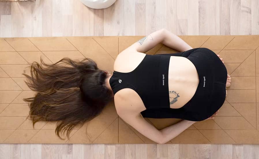 Draufsicht auf Person in entspannter Yoga-Ruhehaltung auf der Matte, Arme angewinkelt und Kopf zur Seite gedreht.
