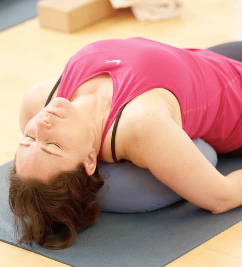 Eine Frau in Sportkleidung liegt entspannt auf einer Yogamatte, gestützt von einem Kissen unter dem Rücken, während sie eine sanfte Yin-Yoga-Position ausführt.