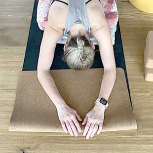 Eine Teilnehmer des Yogaplus-Mini-Retreats kniet zwischen Yogautensilien mit mach vorne aufgelegtem Oberkörper und lang ausgestrecktem Armen auf ihrer Yogamatte und entspannt (Foto: © Yogaplus/Susanne Weisheit)