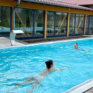 Teilnehmer des Yogaplus-Mini-Retreats schwimmen im beheizten Außenpool oder stehen entspannt im Bademantel mit Drink am Beckenrand vor der Glasfront der Spa-Lounge (Foto: © Yogaplus/Susanne Weisheit)