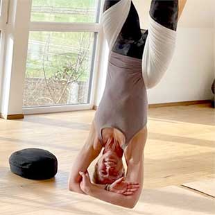 Retreatleiterin Susanne Weisheit hängt entspannt mit verschränkten Armen kopfüber in einem Areal-Yoga-Band von der Raumdecke und lacht in die Kamera (Foto: © Yogaplus/Susanne Weisheit)