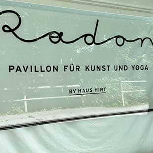 Blick auf das mit weißem Leinentuch von innen verhangene Schaufenster des Yogapavvillions RADON mit Schriftzug 'Radon – Pavillon für Kunst und Yoga' . (Foto: © Yogaplus/Susanne Weisheit)