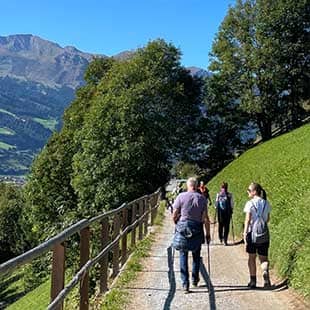 Teilnehmer des Yogaplus Retreats wandern bei strahlend blauem Himmel auf dem Gasteiner Höhenweg mit Blick auf das Hohentauern-Massiv. (Foto: © Yogaplus/Susanne Weisheit)