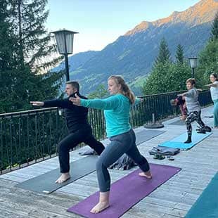 Die Teilnehmer des Yogaplusretreats praktizieren bei nachmittäglichem wolkenlosem Himmel auf der Holzterrasse des Hotels Yogaübungen wie den ‘Sonnengruß‘. (Foto: © Yogaplus/Susanne Weisheit)