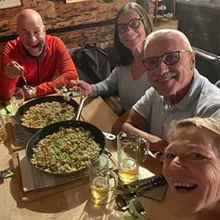 Teilnehmer des Yogaplus Retreats sitzen am Tisch in der urigen Berghütte der Schafflinger Alm und essen „Kasnock’n“ aus zwei großen Eisenpfannen. (Foto: © Yogaplus/Susanne Weisheit)