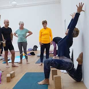Yogalehrerin Susanne Weisheit demonstriert vor Teilnehmern des Yogaplusretreats in einem großen hellen Raum die exakte Ausführung einer Asana. (Foto: © Yogaplus/Susanne Weisheit)