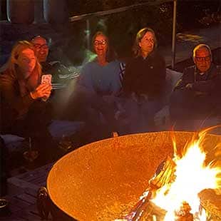 Teilnehmer:innen des Yogaplusretreats sitzen abends bei Feuerschein zusammen auf der Hotelterrasse vor einer riesigen Feuerschale und schauen in die Flammen. (Foto: © Yogaplus/Susanne Weisheit)