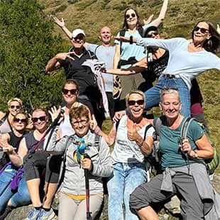 Gruppenbild mit Teilnehmern des Yogaplusretreats in Wanderoutfits, die sonnenbebrillt während einer Wandertour auf einem großen Fels posierend in die Kamera winken. (Foto: © Yogaplus/Susanne Weisheit)