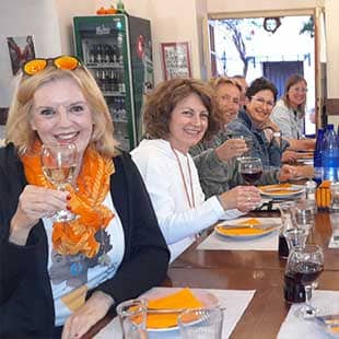 Teilnehmer des Yogaplus Sea & Soul Retreats sitzen zusammen an einer geseckten Tafel in einer griechischen Taverne und prosten mit vollen Bier- und Weingläsern in die Kamera (Foto: © Yogaplus/Susanne Weisheit)