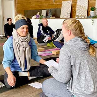 Teilnehmer des Yogaplus Sea & Soul Retreats sitzen sich in einem holzbeplanktem Yogaraum auf ihren Yogamatten gegenüber und meditieren (Foto: © Yogaplus/Susanne Weisheit)