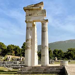 Der Tempel des Asklepios in Epidauros mit Säulenresten eines Porticus vor grüner Baumreihe und blauem Himmel (Foto: © Yogaplus/Susanne Weisheit)