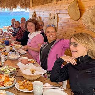Die Teilnehmer des Yogaplus Sea & Soul Retreats sitzen lachend und gut gelaunt auf einer strohgedeckten Holzveranda an der üppig gedeckten Frühstückstafel (Foto: © Yogaplus/Susanne Weisheit)