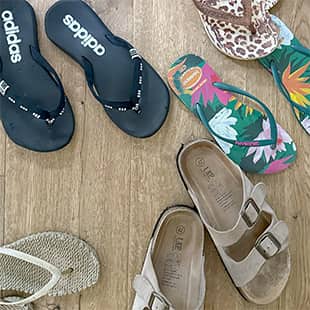 Mehrere bunte Flip-Flops und Sandalen verschiedener Marken liegen verstreut auf einem Holzboden. (Foto: © Yogaplus/Susanne Weisheit)