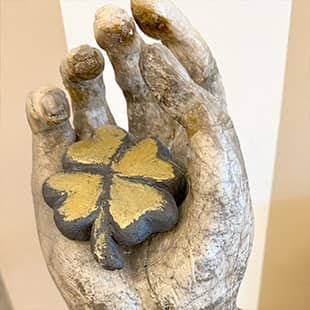 Skulptur einer geöffneten Hand mit einem vierblättrigen Kleeblatt, daneben ein Schild mit der Aufschrift „Du hast Dein Glück in der Hand“. (Foto: © Yogaplus/Susanne Weisheit)