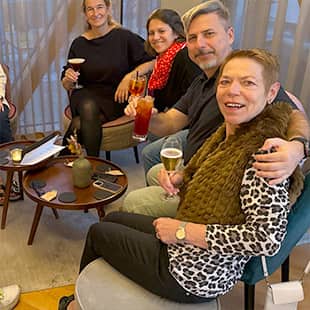 Gruppe von fröhlichen Retreat-Teilnehmern sitzt in Lounge-Atmosphäre im Kreis und stößt mit Cocktails und Biergläsern an. (Foto: © Yogaplus/Susanne Weisheit)