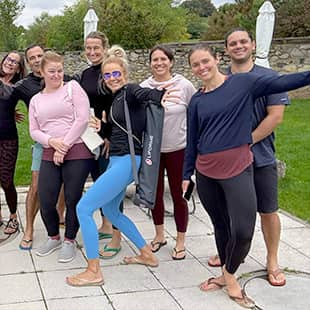 Alle Teilnehmer des Yogaplus-Yogaretreats posieren fröhlich lachend für ein Selfie im Freien auf einer Terrasse von Jordan's Untermühle mit Garten im Hintergrund. (Foto: © Yogaplus/Susanne Weisheit)